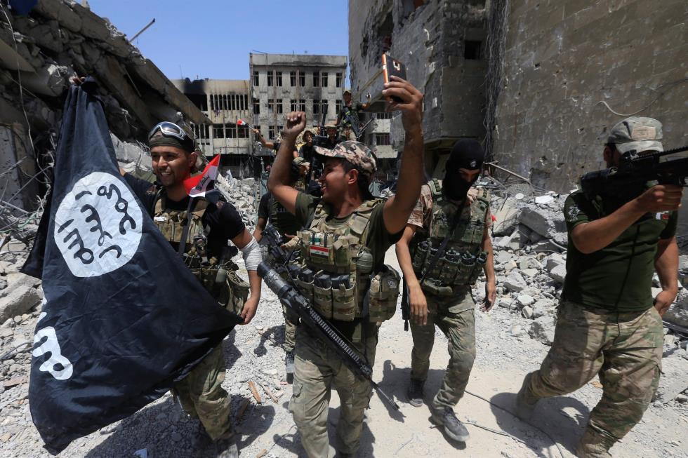 Members of the Emergency Response Division hold an Islamic State flag which they pulled down as they celebrate in the Old City of Mosul