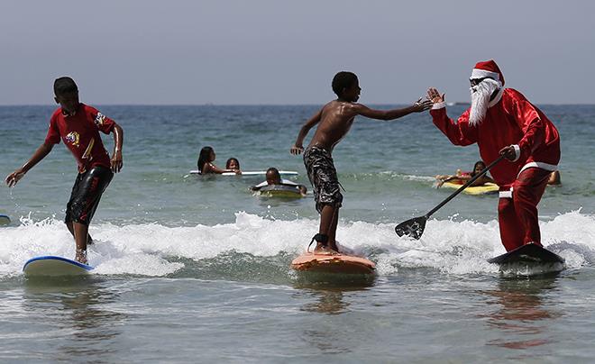 Carlos Bahia, dressed as Santa Claus, jokes with a child as they surf at the Maresias beach, in the state of Sao Paulo